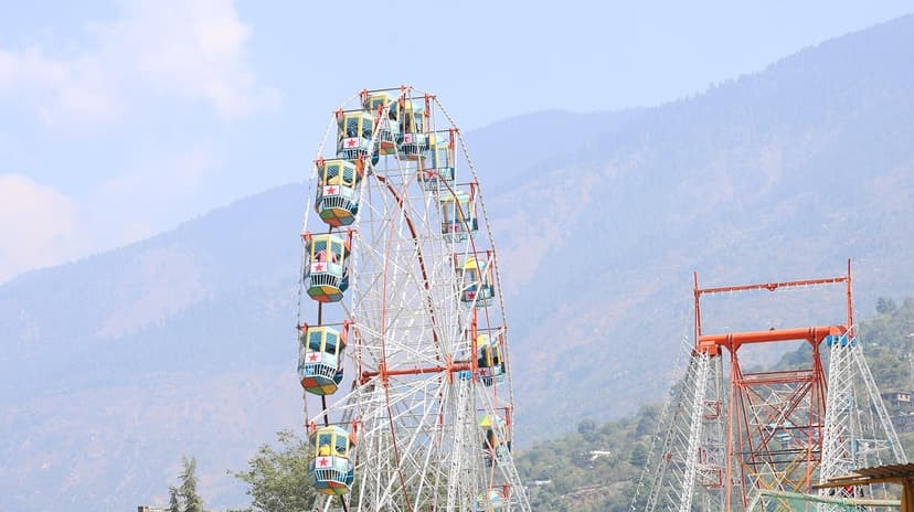 A Ferris wheel at the Kullu Dussehra funfair against forested mountains