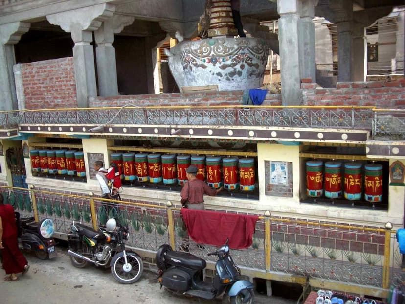 Row of brightly painted Tibetan prayer wheels with stupa above and two people spinning the wheels