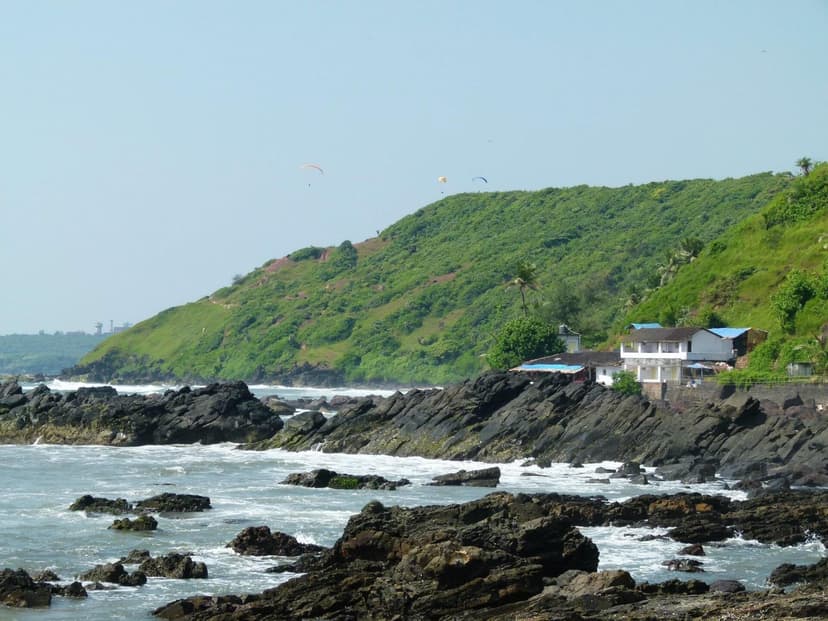 A rocky headland and green cliff on the Arambol coast with paragliders overhead
