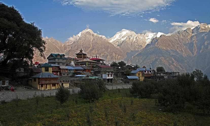 Kalpa village with a wooden temple, traditional houses and a green orchard in front, snow peaks of the Kinner Kailash range behind in soft light