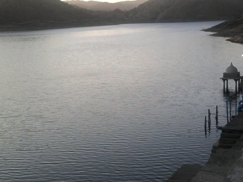 Badi Lake near Udaipur at dusk, calm silver water ringed by the low Aravalli hills, a small stone chhatri pavilion and steps on the right bank