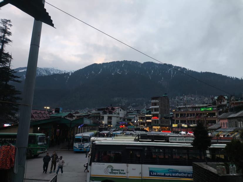 Multiple green HRTC buses parked at Manali bus stand on Mall Road with snow-dusted Dhauladhar peaks behind