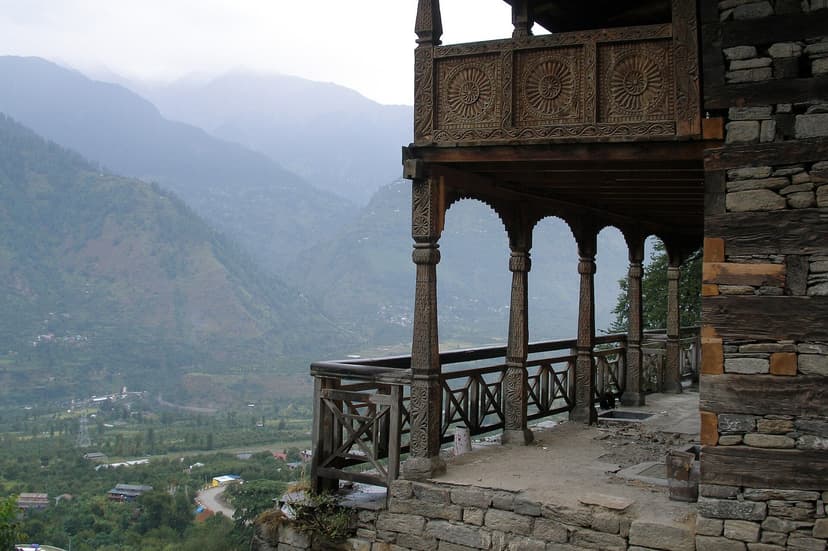 Carved wooden sun-medallion balcony of 15th-century Naggar Castle in stone-and-timber kath-kuni style, overlooking the green Kullu Valley below