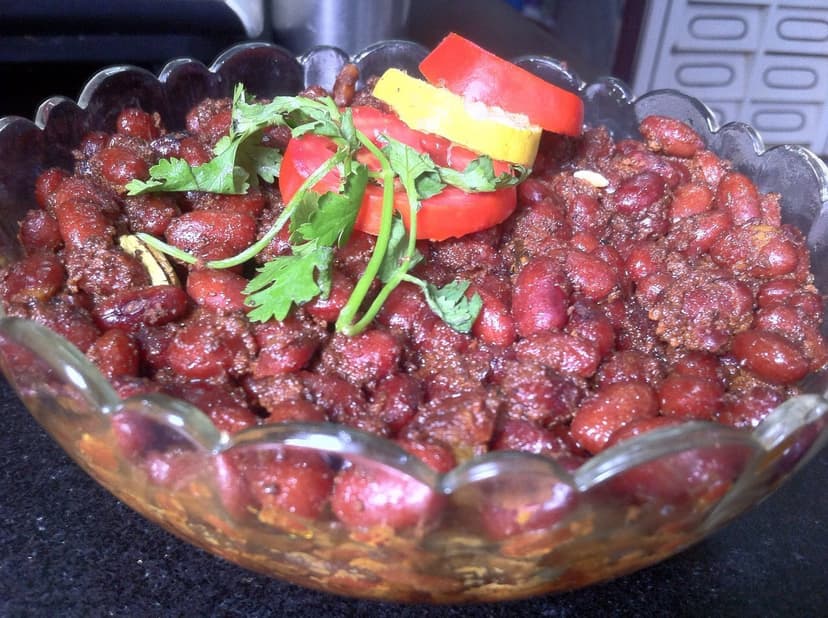 Dark red Chamba rajma kidney beans in a glass serving bowl garnished with coriander and tomato, the famously small dark variety that Chamba district is known for