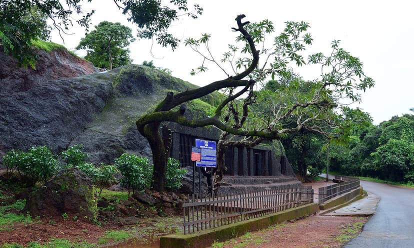 The Arvalem cave site seen from a quiet road, with an old tree and a signboard