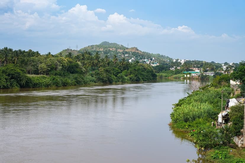 A wide river swollen brown with monsoon runoff, running between green forested banks and hills