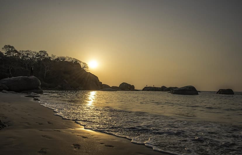 Sunset at Agonda Beach, South Goa: low sun over a rocky headland, gentle surf and footprints in the sand