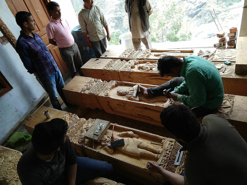Himachali woodcarvers cutting relief figures into temple beams during a reconstruction