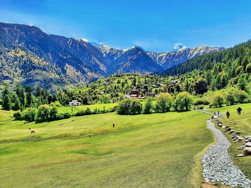 Wide Shangarh meadow with a stone walking path, a hillside village and snow peaks behind