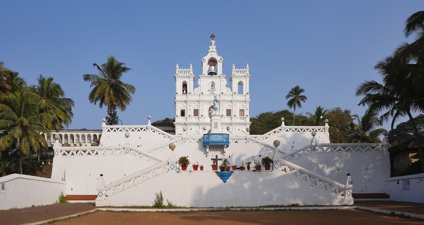 The large white Baroque Church of Our Lady of the Immaculate Conception in Panjim, Goa, with a tall central belfry and symmetrical zigzag stairways climbing to it under a blue sky.