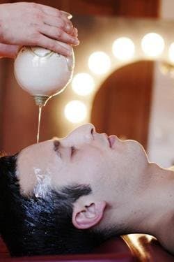 Warm oil poured in a thin stream onto the forehead of a person lying down, a shirodhara treatment