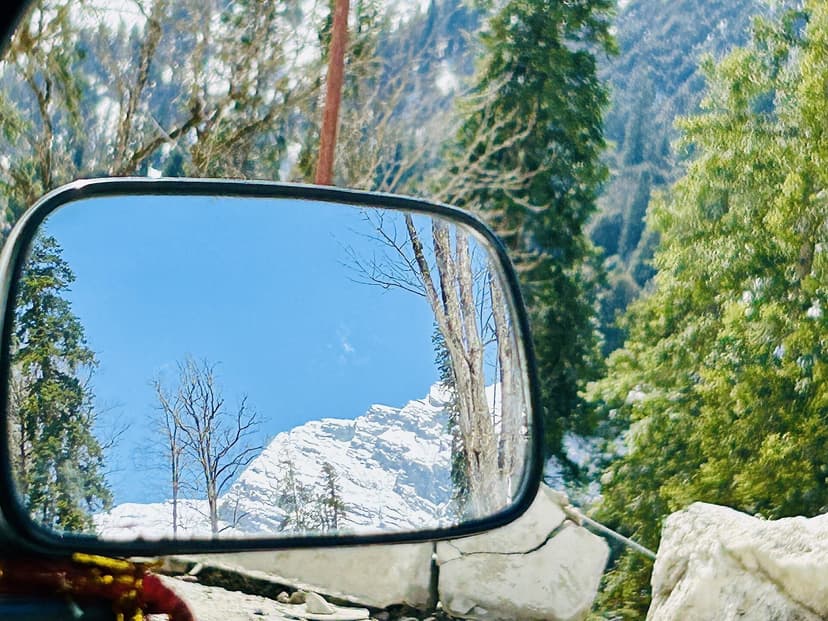 A snow peak reflected in a car wing mirror on the mountain road above Manali