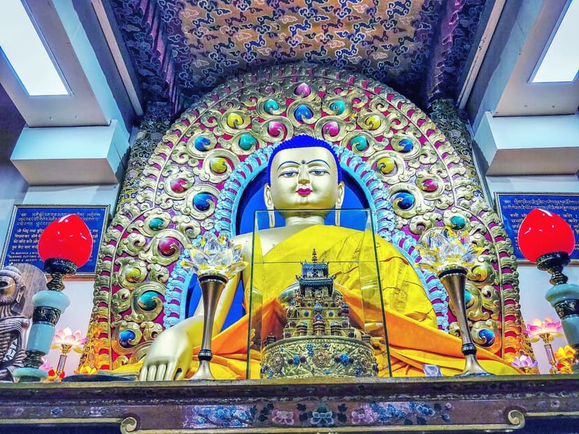 Bright Buddha statue inside the Tsuglagkhang complex (Dalai Lamas main temple) in McLeod Ganj — colourful aureole, gold drape, ritual lamps