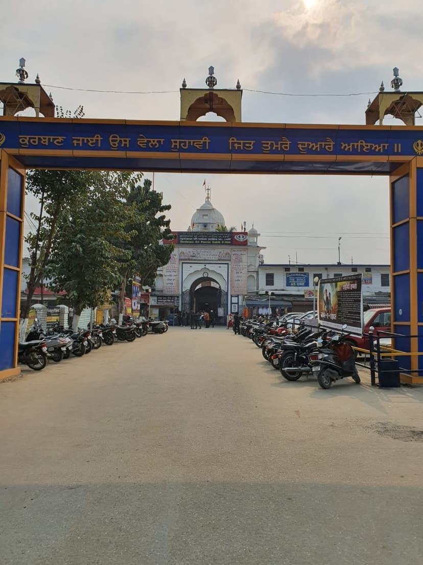 Entrance gateway of Gurdwara Sri Paonta Sahib with Gurmukhi inscription and the white dome of the main shrine behind, parked motorcycles lining the approach