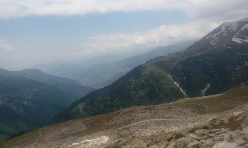 View from Sach Pass in Chamba district looking towards the green Pir Panjal range with misty valleys below and rocky terrain in the foreground