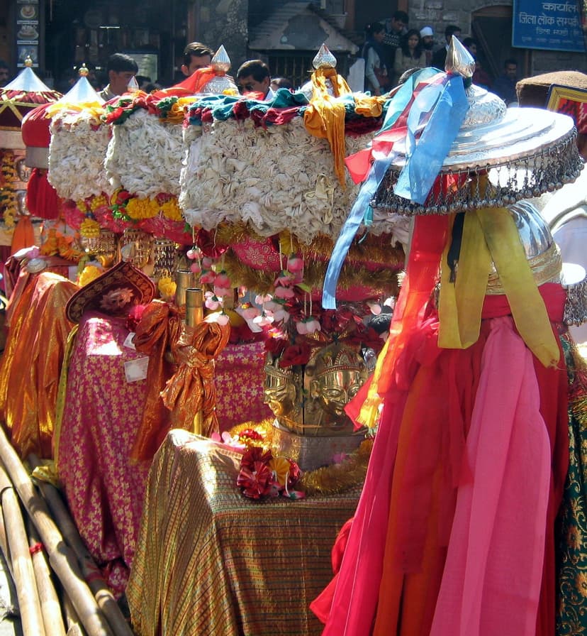 Decorated village deity palanquins draped in red and orange cloth with silver mohra masks at the Mandi International Shivratri Fair