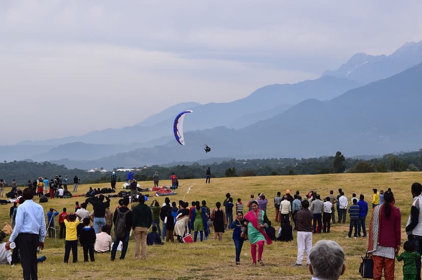 Crowd at the Bir landing field during the Paragliding World Cup 2015, with a single paraglider on final approach and Dhauladhar peaks behind