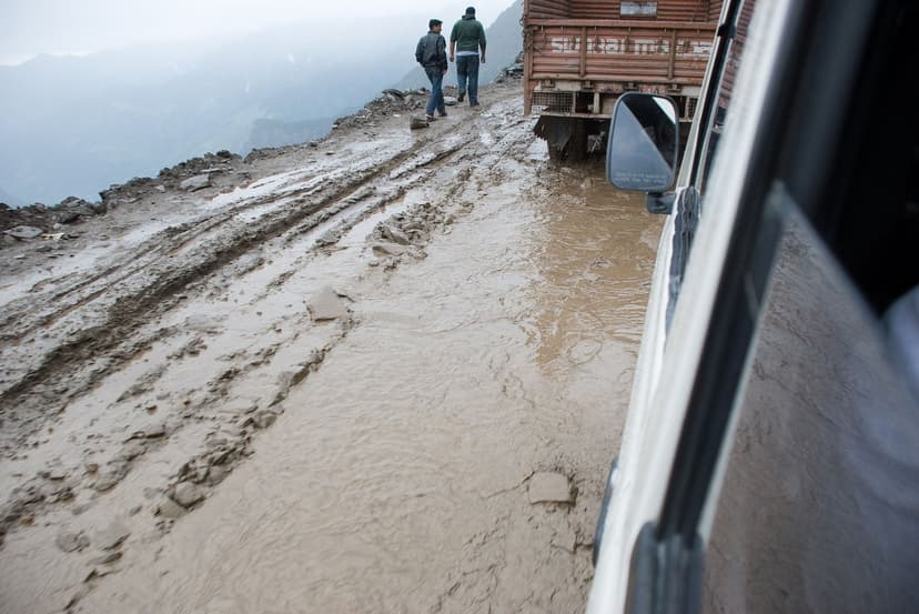 Axle-deep mud and slush on the road to Rohtang Pass photographed from a vehicle window, with a truck ahead and two people walking through the muck