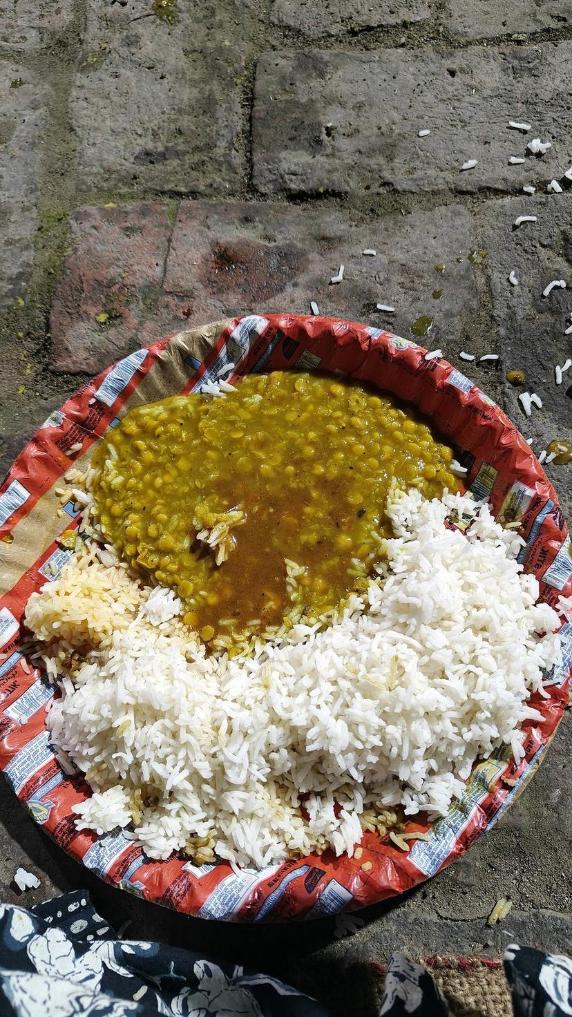 A served Kangri Dham of yellow chana dal and white rice on a disposable plate placed on stone, photographed at a temple in Himachal Pradesh — community feasts often serve hundreds of plates this way during festivals and family events