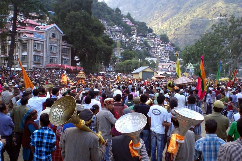 Kullu Dussehra festival procession showing decorated deity palanquins being carried by crowds through the town, colourful flags and festive atmosphere