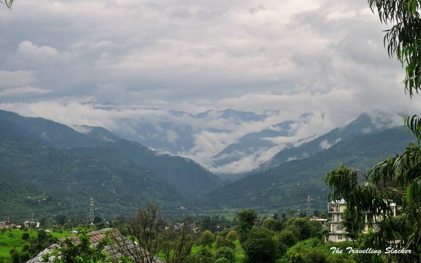 Cloud pouring through the forested ridges of Karsog valley with scattered houses and trees in the foreground