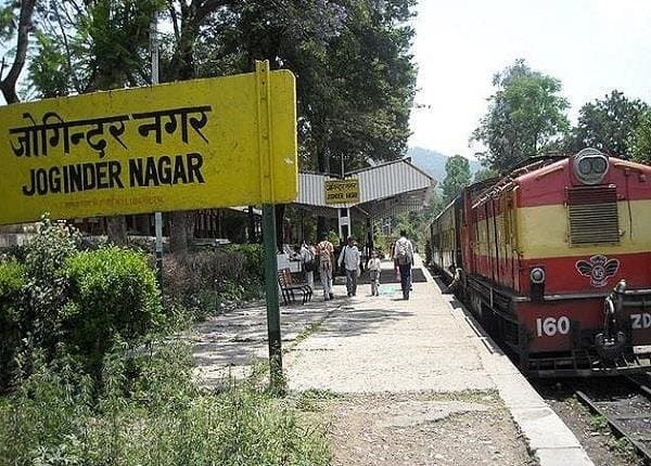 Yellow Joginder Nagar station signboard in Hindi and English with a red ZDM-class diesel locomotive at the platform behind
