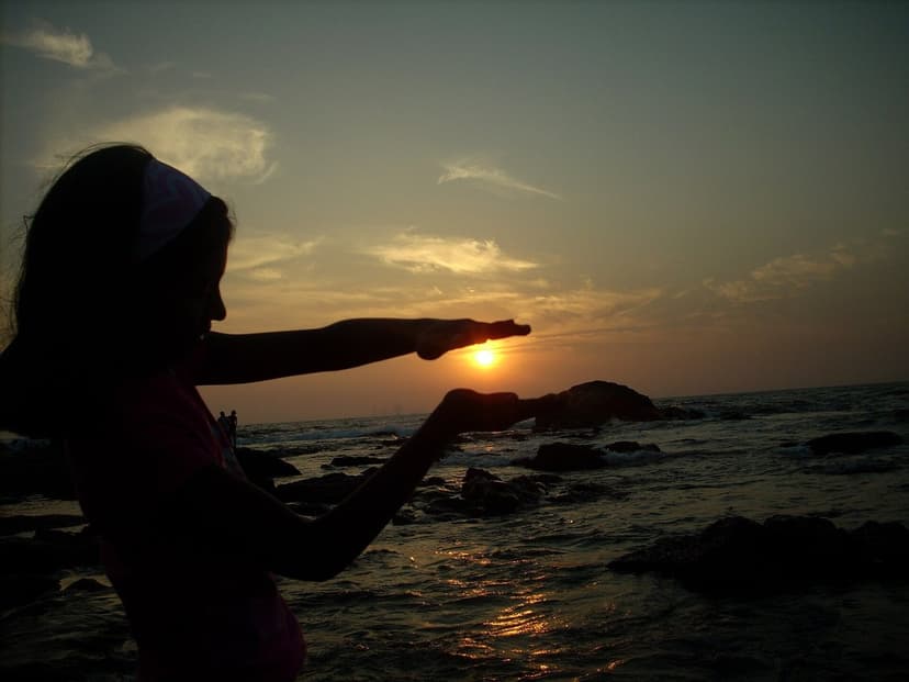 A person silhouetted on the rocks at Anjuna framing the setting sun with their hands