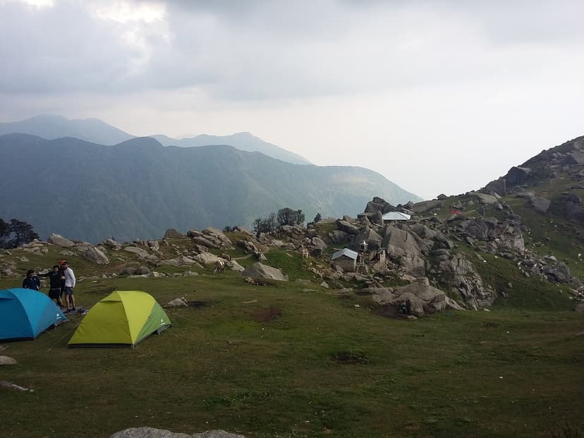 Two dome tents pitched on a high Himalayan meadow with rocks scattered around and the Dhauladhar ridge visible behind