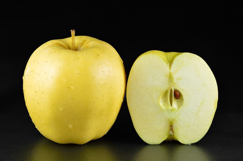 A whole Golden Delicious apple beside a cross-section showing pale flesh and a single dark seed — the variety Florence Stokes shipped to her son from Philadelphia as a Christmas gift
