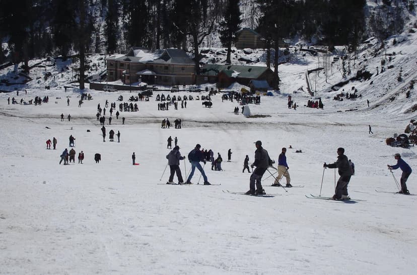 People skiing and standing on a snow slope at Solang Valley, Manali, with the iconic resort building and pine ridge in the background