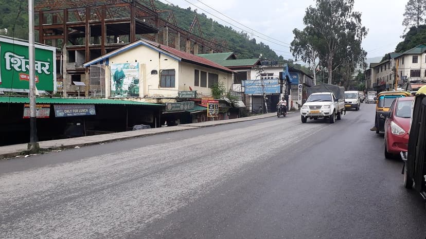 A street in Mandi town with shops, hoardings in Hindi, parked cars and an SUV passing