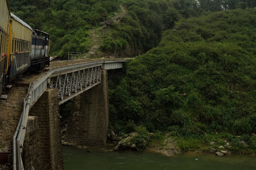 View from inside a Kangra Valley Railway coach as the train crosses a stone-and-girder bridge over a river near Baijnath