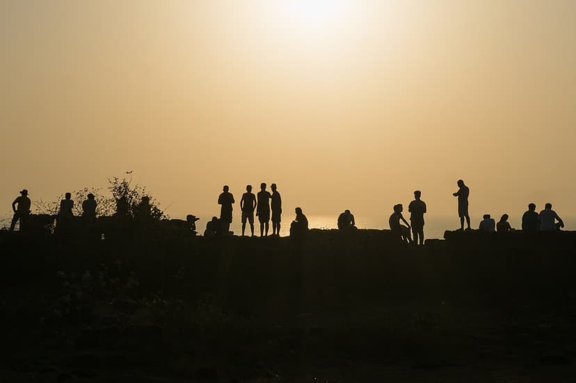 Silhouettes of a crowd standing on the ramparts of Chapora fort against a golden sky