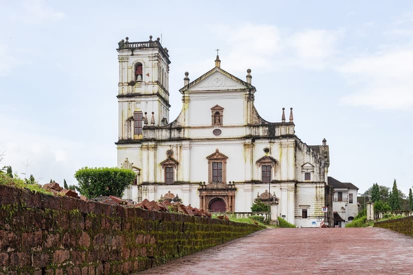 The large white Se Cathedral in Old Goa seen from the old Rua Direita, its single surviving bell tower on the left, a laterite wall in the foreground