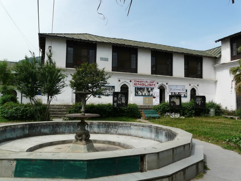 White facade of Akhand Chandi Palace in Chamba with arched doorways and a dry fountain in the courtyard, now a government college
