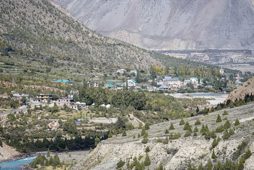 Jispa village in Lahaul with colourful rooftops spread across a wide valley floor alongside the Bhaga river, barren grey peaks behind