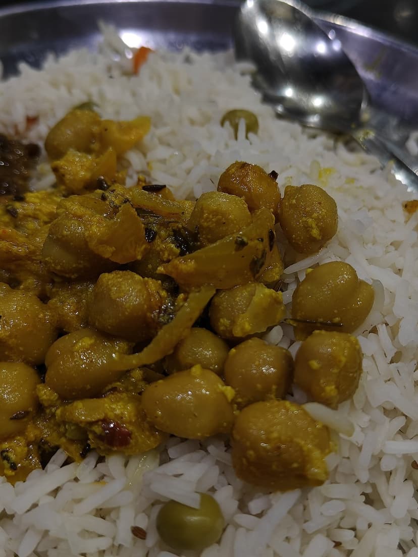 Close-up of White Chana Madra (chickpeas slow-cooked in yoghurt with green peas) served over basmati rice on a steel plate — a signature dish of Kangri Dham prepared by Boti hereditary chefs in Himachal Pradesh