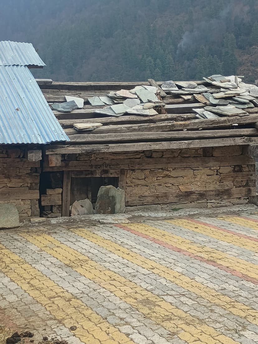 An abandoned traditional Himachali house with slate stone roof on wooden rafters next to a corrugated metal replacement — showing the slow disappearance of kath-kuni construction in HP villages