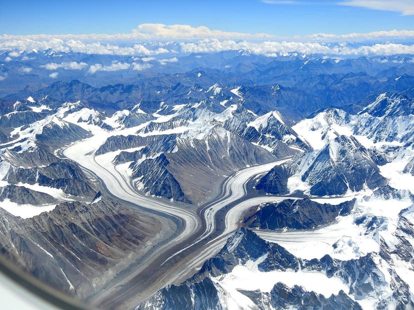 Aerial view of two long ice tongues coming off the central Himalayan ridge into a valley, dark medial moraine stripes running down the middle of each glacier, snow peaks behind, classic glacier-feeder pattern