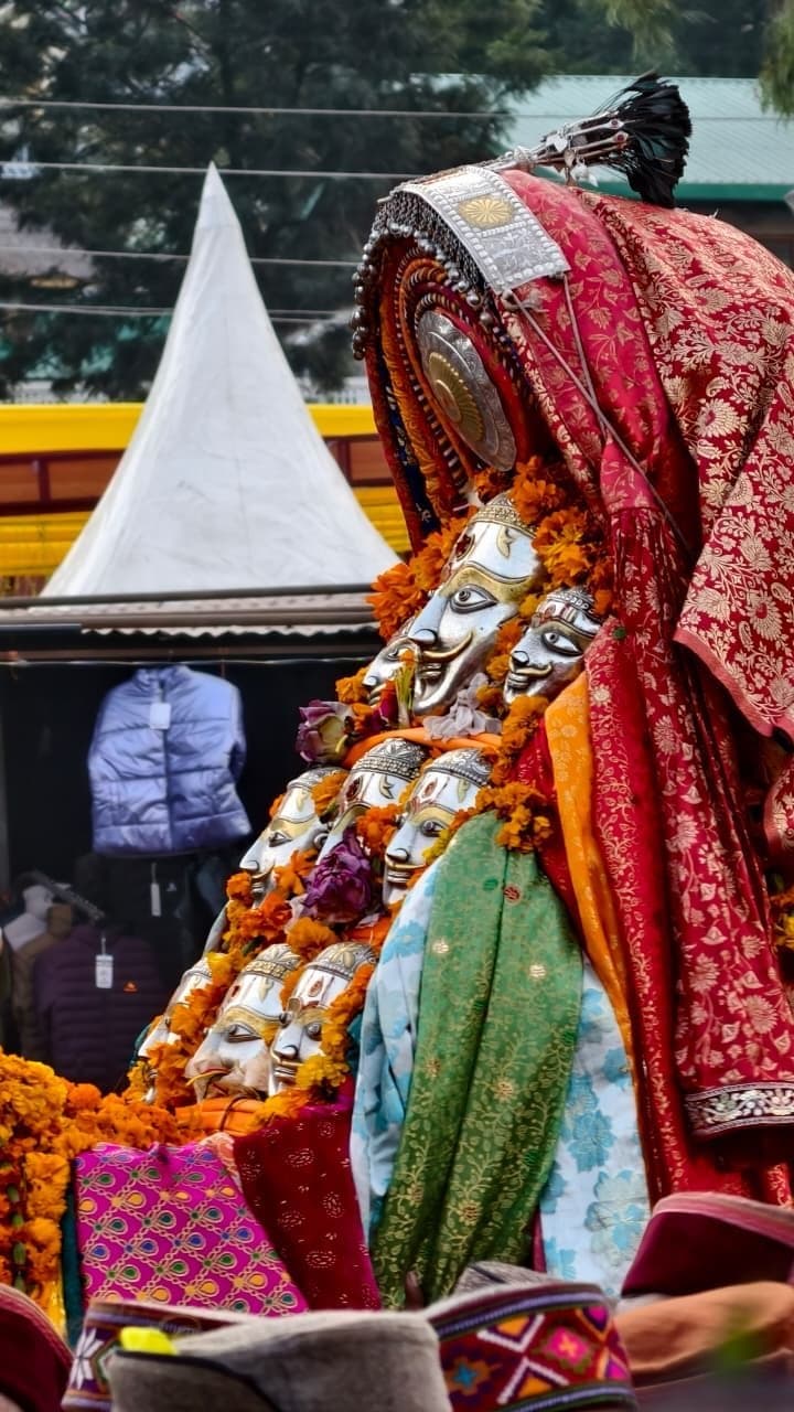 Silver deity masks of a Kullu devta arrayed on a palanquin draped in brocade and marigolds during a festival
