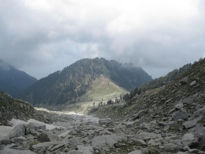 View down a wide rocky valley toward a forested ridge with clouds, the Laka Got section