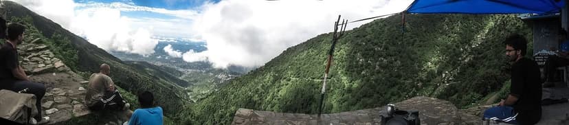 Panorama from Magic View Cafe looking over Kangra Valley with trekkers seated on stone wall