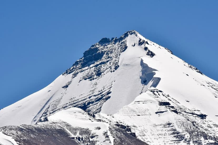 A snow-streaked Himalayan peak in Spiti against a clear deep-blue sky with rocky lower slopes and a fresh wind-blown ridge of snow on the summit