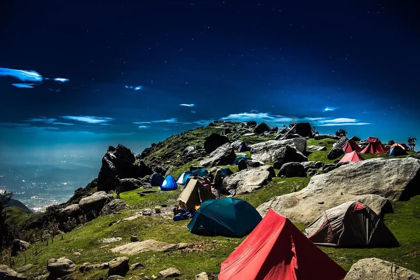 Night camping at Triund: tents on rocky meadow with stars overhead and valley lights below